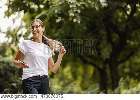 A Happy Girl Walking In The Public Park, Spending The Day In Nature, And Listening To Her Favorite R