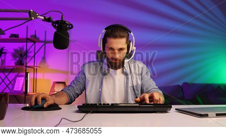 Cybersportsman In A Neon Room. Gamer Bearded Guy, In Gaming Headphones, Challenges. Lifestyle Gamer,