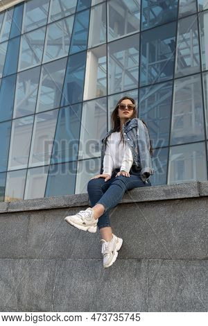 Young Woman In Sunglesses In Youth Clothing On The City Street. Attractive Stylish Woman Resting On 