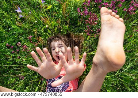 Portrait Of A Child Girl In Summer Lying In The Grass And Wildflowers With Heels And Palms. Summer T