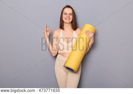 Portrait Of Pretty Positive Athletic Woman Holding Rolled Up Fitness Mat And Showing Okay Sign Appro