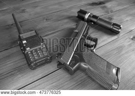 A Walkie-talkie, A Gun And A Flashlight On A Wooden Table. Weapons And Military Equipment. Black And