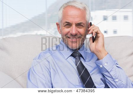 商人在智能手机上调用和 staffroom 在沙发上的照相机在微笑