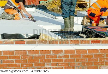 Builder Placing Polystyrene Insulation Boards On Waterproofing Membrane During Floor Construction. E