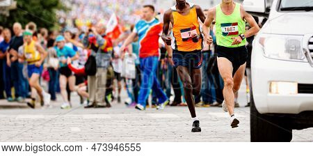 Two Leading Runners Kenyan And European Running Marathon Behind An Escort Car, Jogger Run World Cham