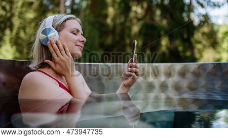 Reaxed Woman With Headphones Listening To Music In Outdoor Bathtub.