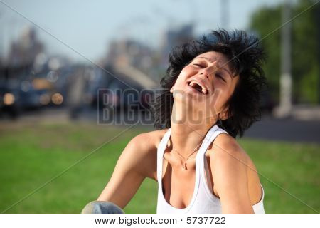 Laughing Girl Sits On Lawn At Road In City