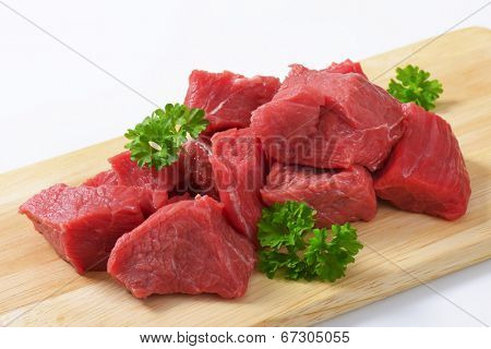 heap of diced beef meat with pieces of parsley, served on the wooden cutting board 