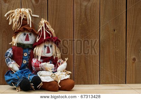 Scarecrows sitting by rustic wooden fence