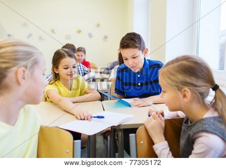 education, elementary school, learning and people concept - group of school kids with pens writing test and showing notebook in classroom