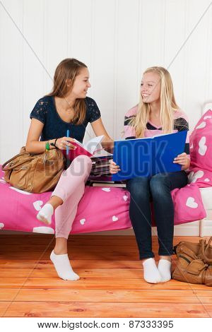 two teengirls sitting on bed making homework together