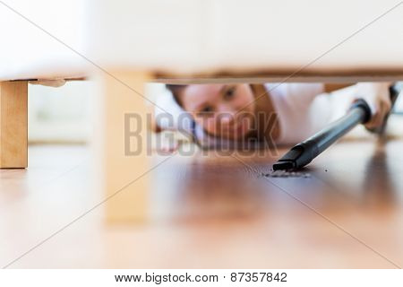 people, housework and housekeeping concept - close up of happy woman with vacuum cleaner cleaning floor under couch at home