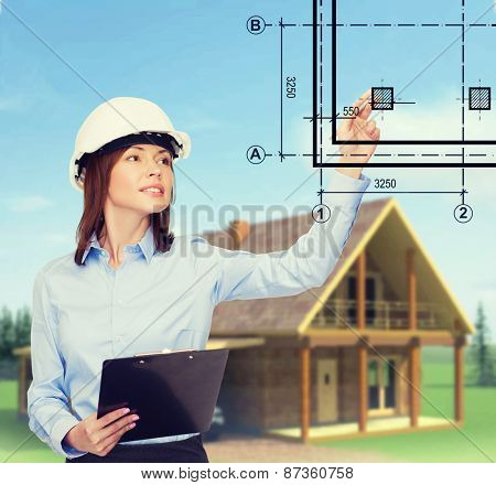building, developing, consrtuction and architecture concept - smiling businesswoman in white helmet with clipboard pointing finger
