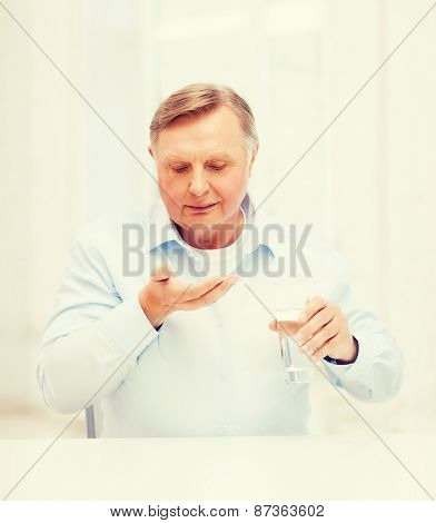 healthcare, madicine, pharmacy and elderly concept - old man with pills and glass of water