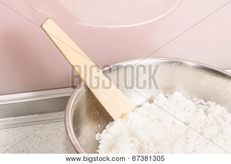 Cooked white rice in a metal bowl and wooden spoon stirrer