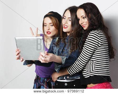 Three girls friends taking selfie with digital tablet, studio shot over gray vackground