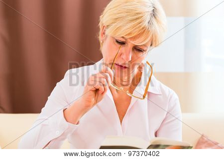 Old woman reading  book at home with glasses