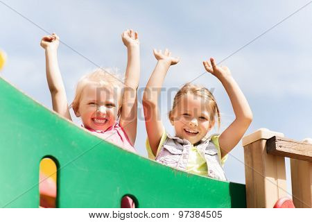 summer, childhood, leisure, friendship and people concept - happy little girls waving hands on children playground climbing frame