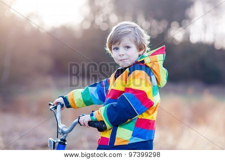 Kid Boy In Safety Helmet And Colorful Raincoat Riding Bike, Outd
