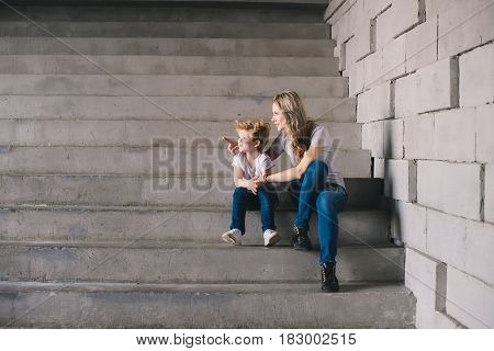 Mother with son sitting on a stairs and looking somewhere