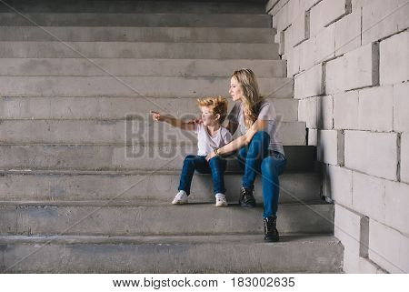 Mother with son sitting on a stairs and looking somewhere