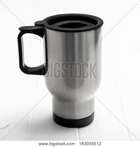 Huge lovely metallic thermocup with black comfortable handle on side, sitting on table
