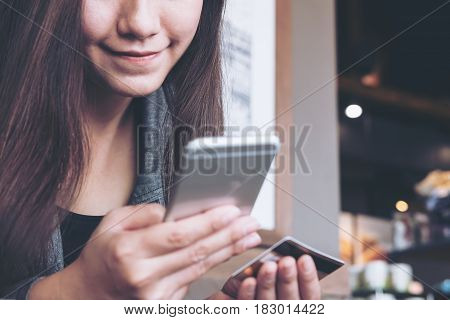 A smiley face Asian woman holding credit card and mobile phone in office with feeling happy