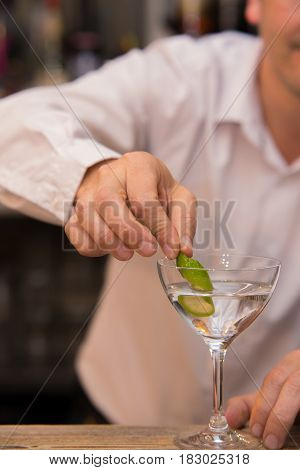 Closeup of barman hand putting lemon peel on a glass to prepare cocktail.