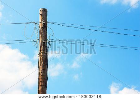 Old wooden pillar with power line against the blue sky. A botched electrical connections