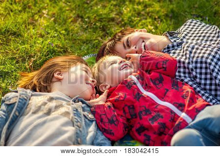 Mom and two kids lie on the grass in the park, laugh, spring, family