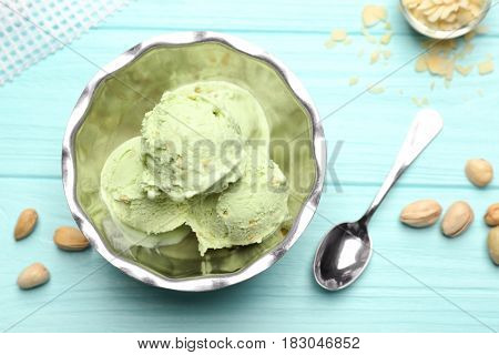 Tasty pistachio ice cream in bowl and nuts on wooden table