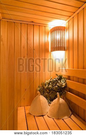 Interior of a sauna . Advantage for health. Oak brooms for a steam room in traditional russian wooden bath. Leaf Venik With Dried Herbs in wooden sauna bucket and sauna hat.