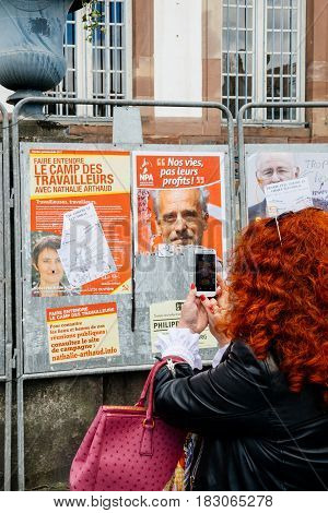 STRASBOURG FRANCE - APR 23 2017: Woman taking on mobile phone Presidential campaign posters of candidates fro French presidency