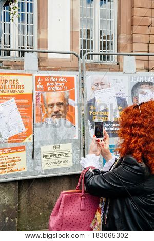 STRASBOURG FRANCE - APR 23 2017: Woman taking on mobile phone Presidential campaign posters of candidates fro French presidency