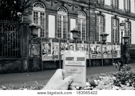 STRASBOURG FRANCE - APR 23 2017: Man holding Carte Electorale - voter's card French voter registration card in front of official campaign posters for all eleven candidates for the 2017 French presidential elections outside pooling station