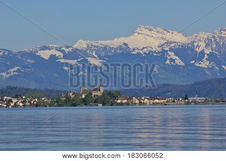 Spring scene at lake Zurichsee. Medieval castle in Rapperswil. Grosser Speer snow capped mountain.