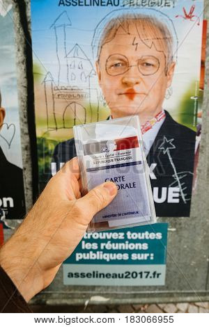 STRASBOURG FRANCE - APR 23 2017: French voter registration card held by male hand in front of official campaign poster of Francois Asselineau candidate for the 2017 French presidential elections posted outside a polling station
