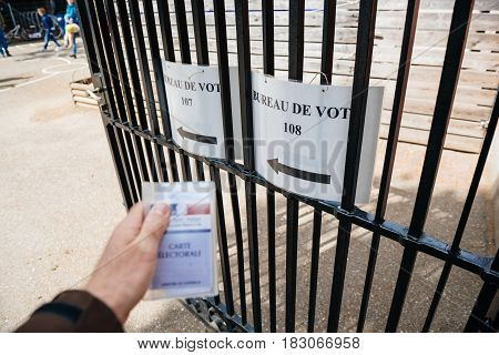 STRASBOURG FRANCE - APR 23 2017: French voter registration card held by male hand in front of Bureau de Vote Voting Section open for the 2017 French presidential elections posted outside a polling station