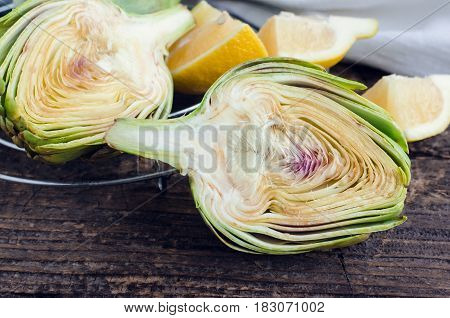 Ripe fresh organic artichokes with lemon and white napkin on rustic wooden background.