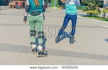Two girls rollers go one after another in sunny day. Back view