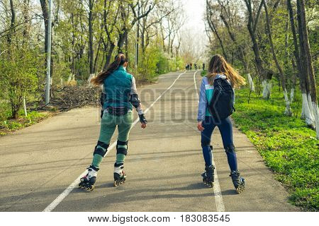 Two girls on roller skates ride along the road next to each other. Sport girls.