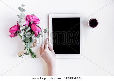 Modern spring design with bright pink flowers and tablet in hand on white desk background top view moke up