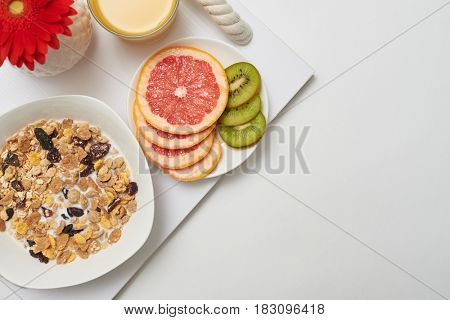 Cropped shot of a bowl of corn flakes, fruits and orange juice on tray, flay lay. White background 