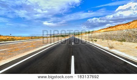 Long highway crossing sunny desert wind under dramatic sky summer day