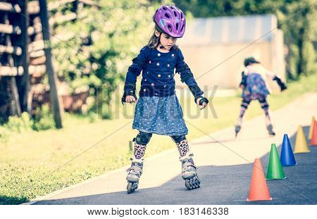 Children Learning To Roller Skate On The Road With Cones.