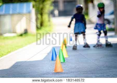 Children Learning To Roller Skate On The Road With Cones.