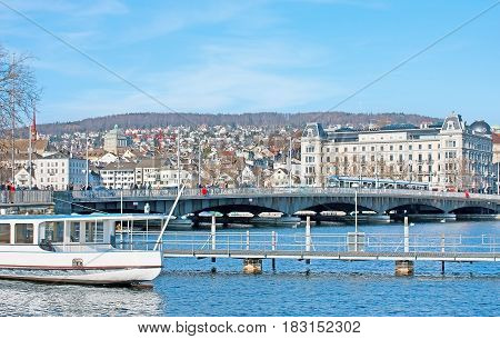 ZURICH SWITZERLAND - MARCH 20 2011: The walk along the Zurichsee (Zurich lake) with the view on the Quaibrucke bridge and the buildings of old town on March 20 in Zurich.