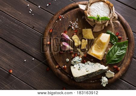 Cheese delikatessen top view on rustic wood. Wooden desk with blue cheese roquefort, parmesan, camembert and brie cuts decorated with garlic, pomegranate and rosemary.