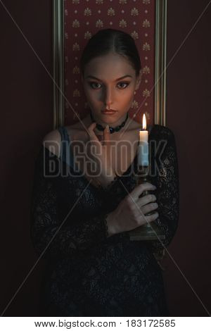 Beautiful and sad woman in a dark room with a candle.