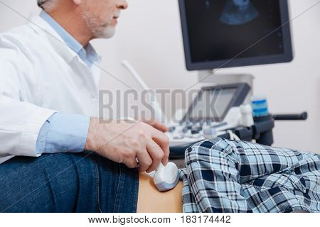 Monitoring echo waves in the body. Charismatic attentive aged practitioner working in the hospital while providing ultrasonic abdomen monitoring and using ultrasound equipment